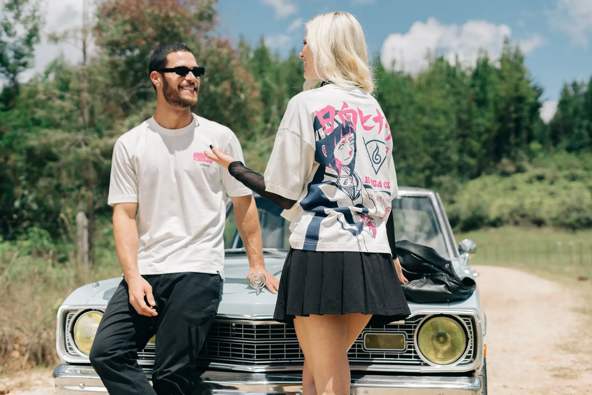 Fotografía editorial de la campaña TU PAR: pareja apoyada en el capó de un auto clásico, ella con top de estampado anime y él con camiseta blanca y gafas de sol.