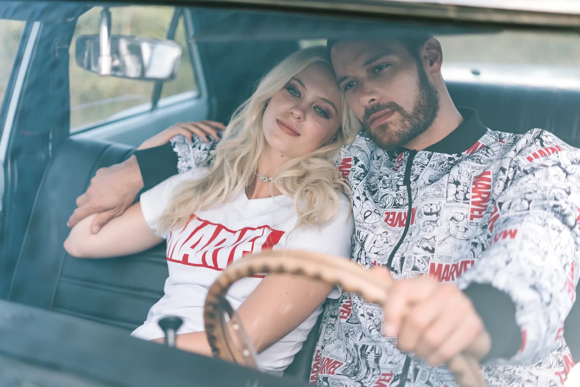 Fotografía editorial de la campaña TU PAR: pareja dentro de un auto clásico, ella con camiseta blanca de Marvel y él con camisa de estampado de cómic al volante.