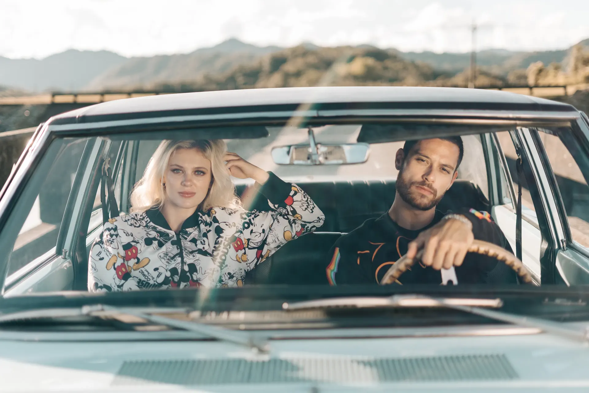 Fotografía editorial de la campaña TU PAR: la pareja en los asientos delanteros de un auto clásico, ella con camisa de estampado de cómic y él conduciendo.