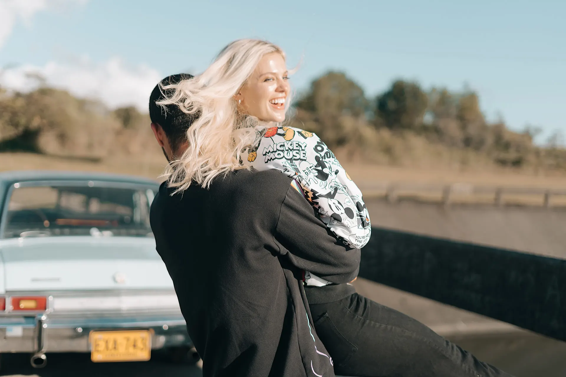 Fotografía editorial de la campaña TU PAR: el hombre abraza a la mujer, que sonríe, junto a un auto clásico, ella con un top de estampado de cómic.